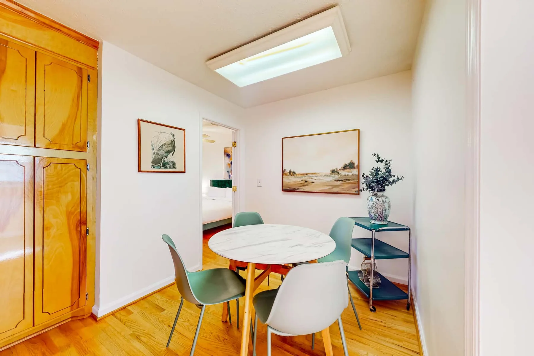 A dining area with a round table, green seating, and framed artwork.
