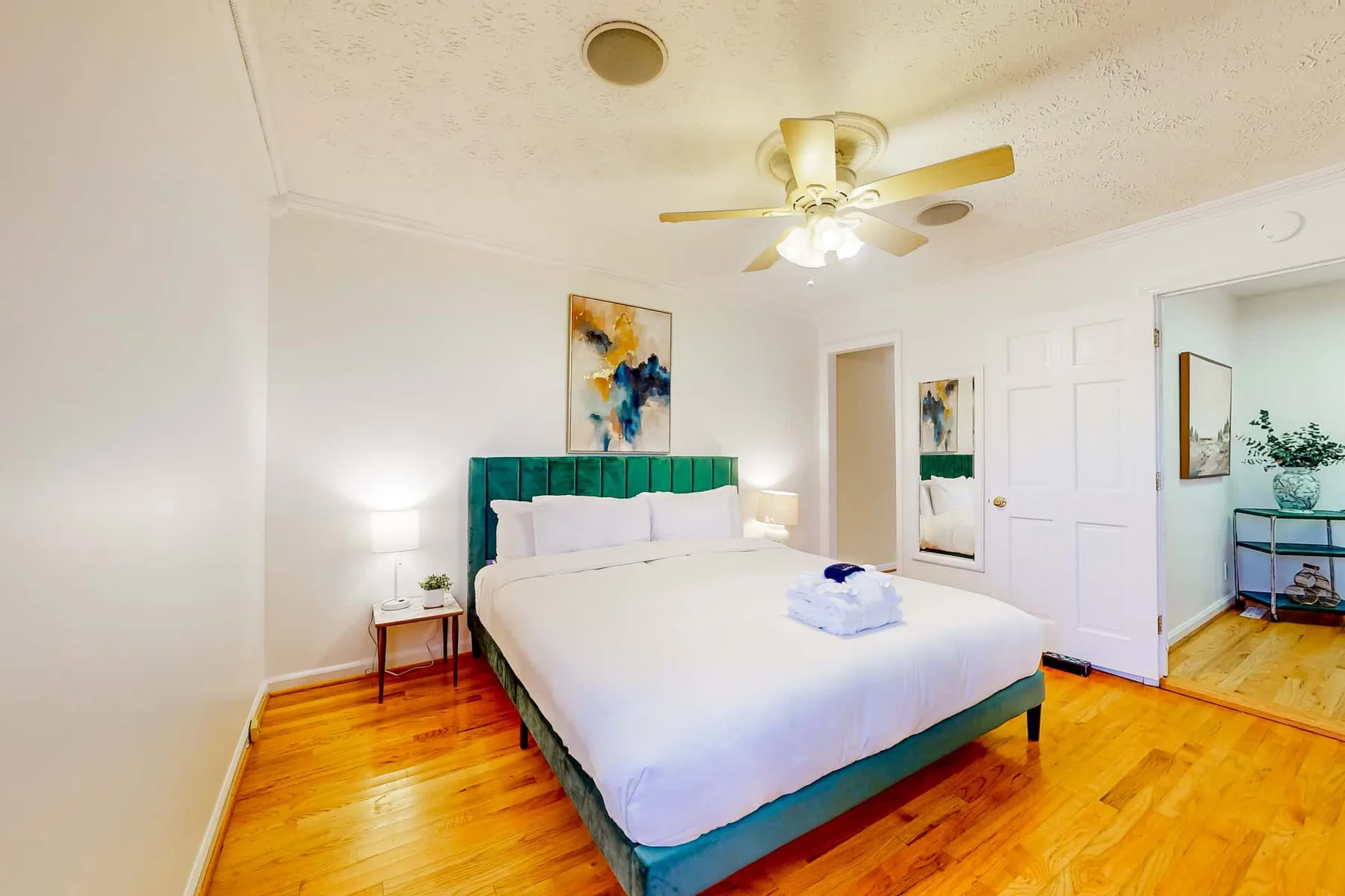 A bedroom with a bed, teal headboard, and polished wood flooring.