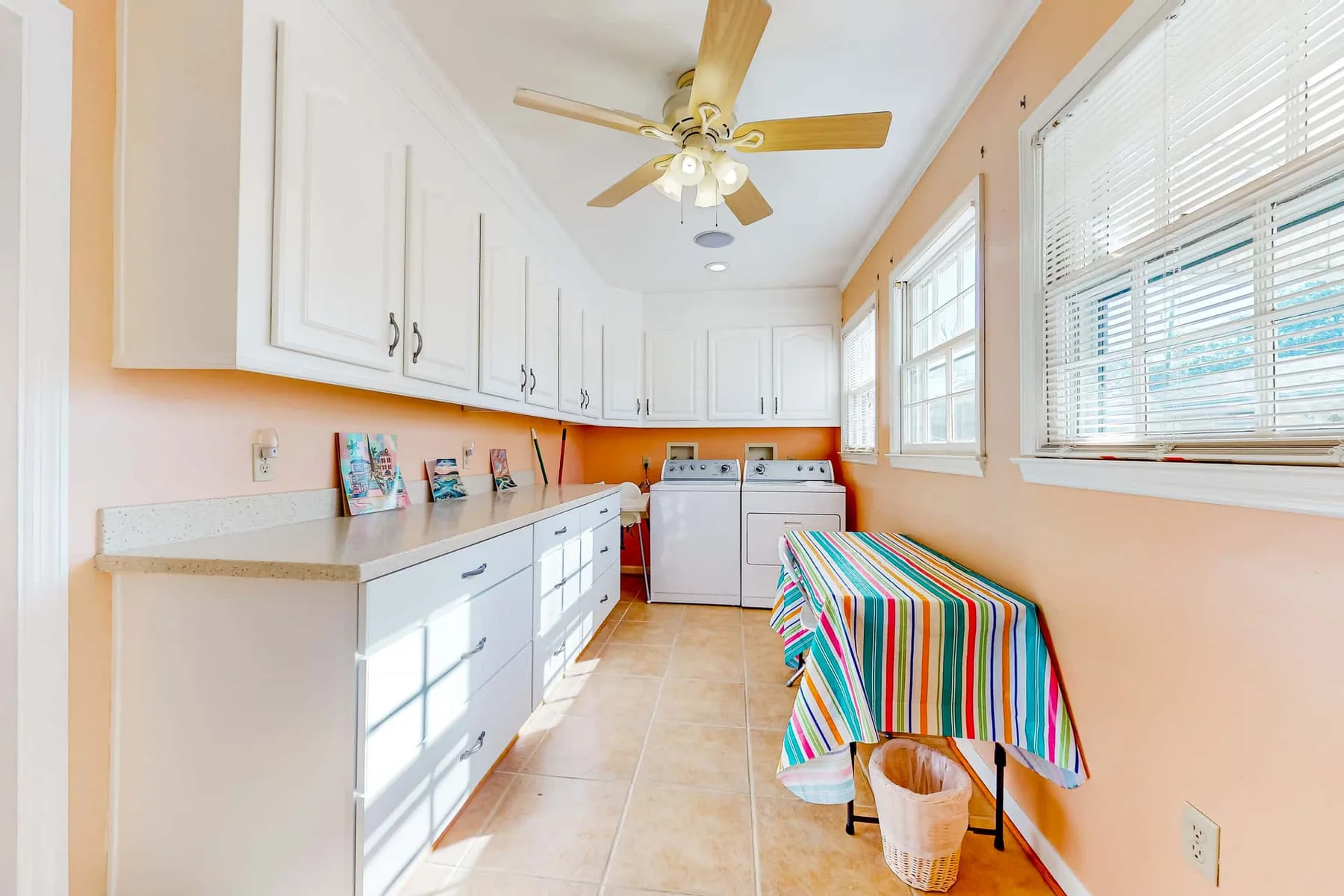 A bright kitchen with white cabinets, appliances, and a colorful tablecloth.