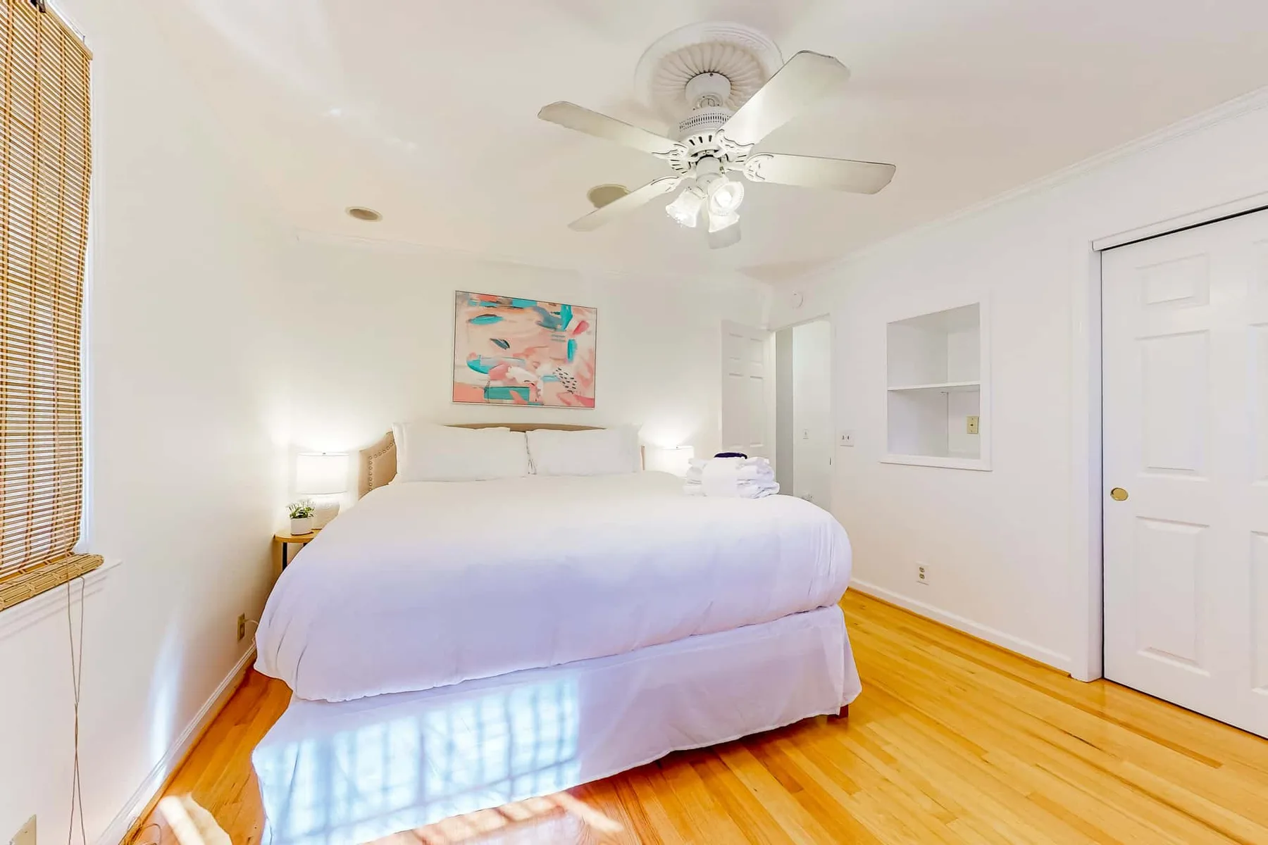 A bright bedroom with a bed, wooden flooring, and a ceiling fan.