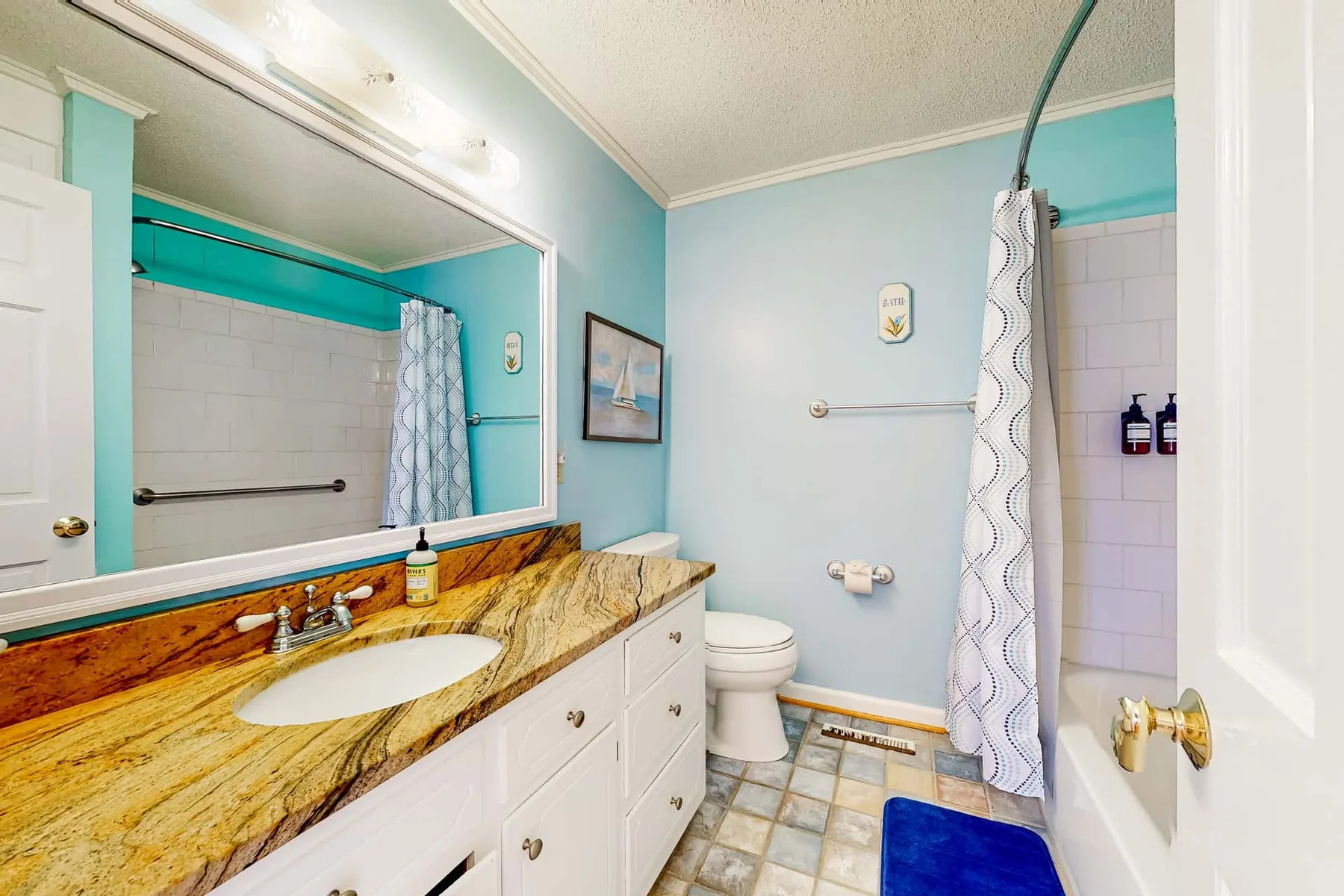 A bathroom with a long vanity, mirror, toilet, and shower curtain.