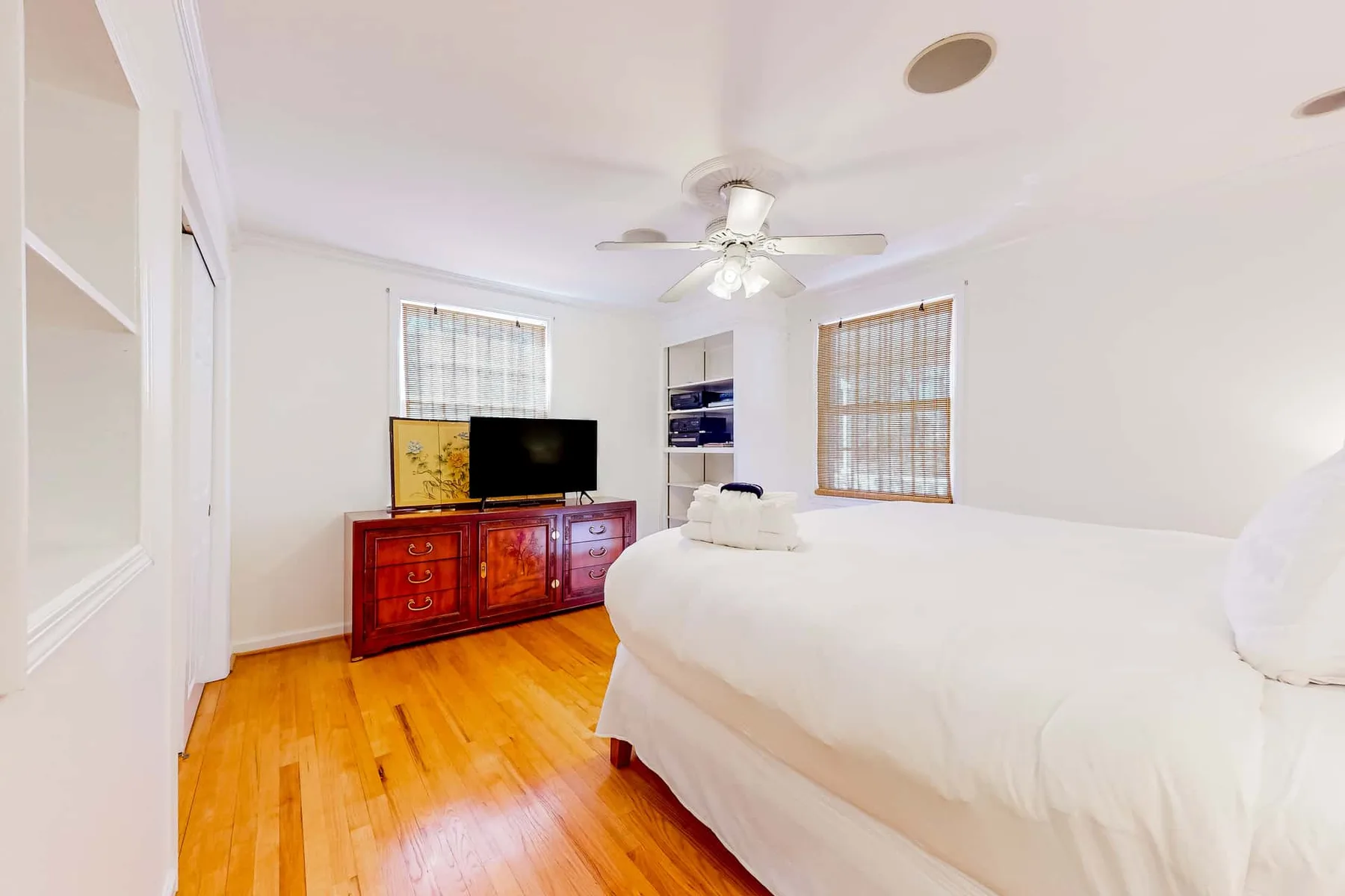A bright bedroom with a large bed, wooden dresser, and ceiling fan.