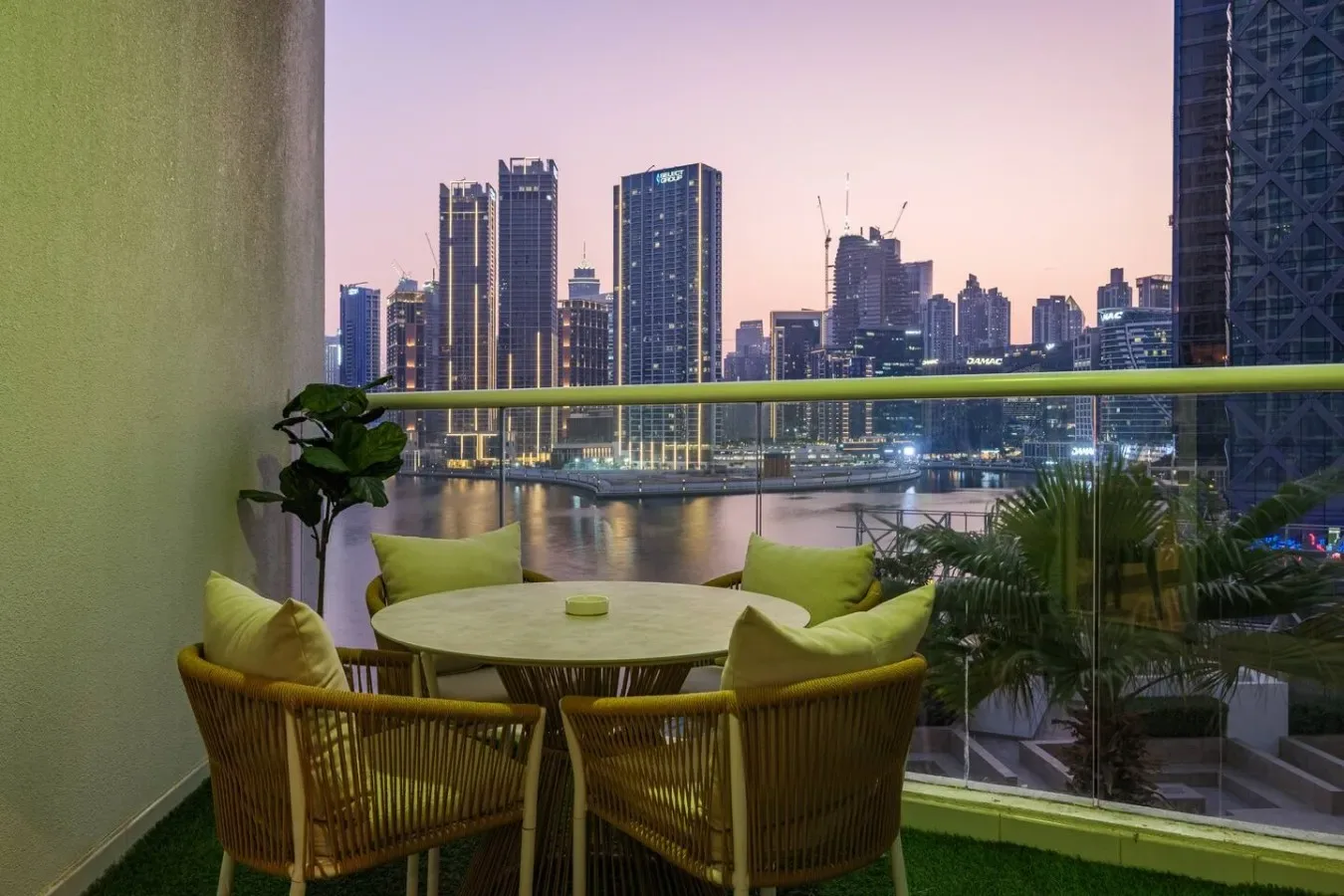 Una zona de estar en el balcón da a un río y al horizonte urbano iluminado al anochecer.