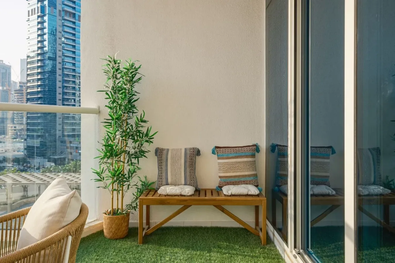 Una zona de descanso en el balcón con un banco de madera, cojines y una planta en maceta.