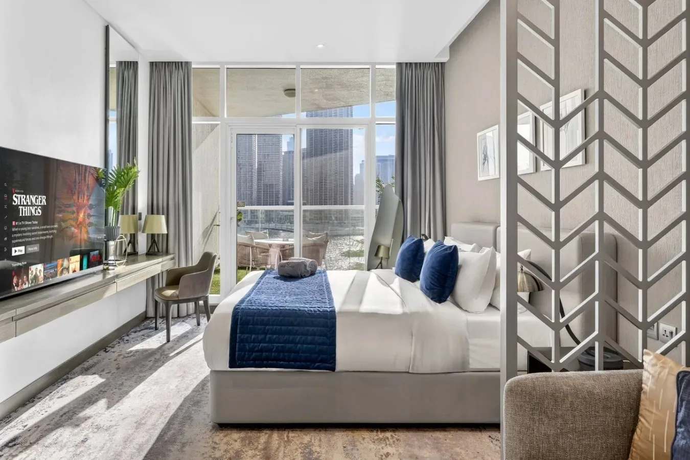 Un dormitorio luminoso con una cama, ropa de cama azul y ventanales.