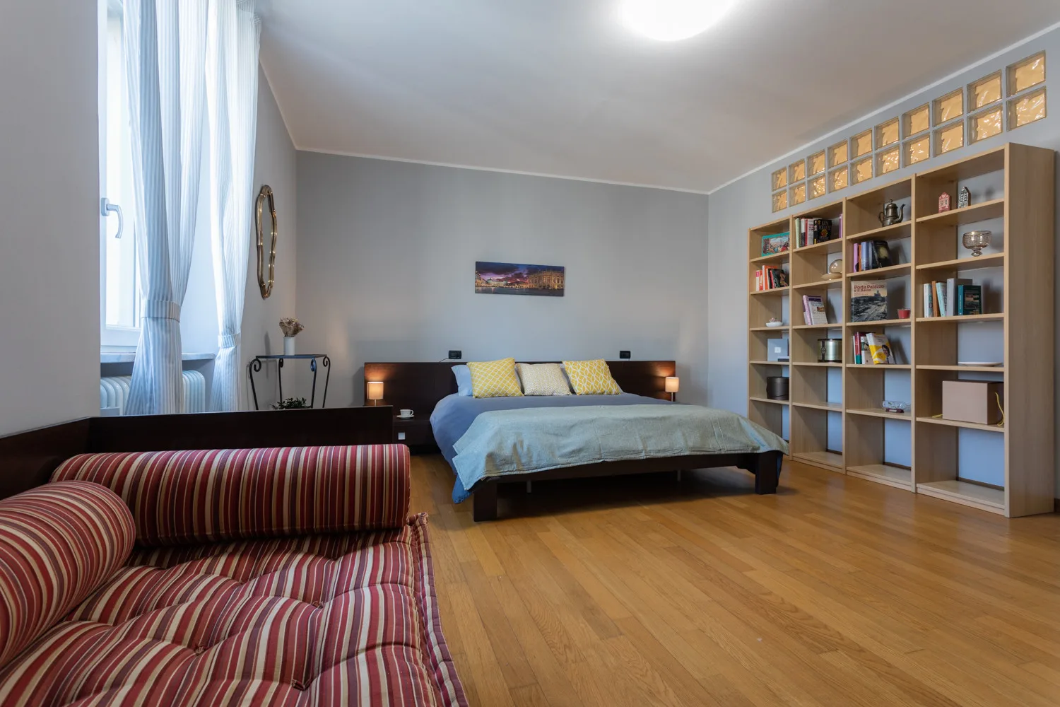 Un dormitorio con una cama, una estantería y un sofá a rayas.