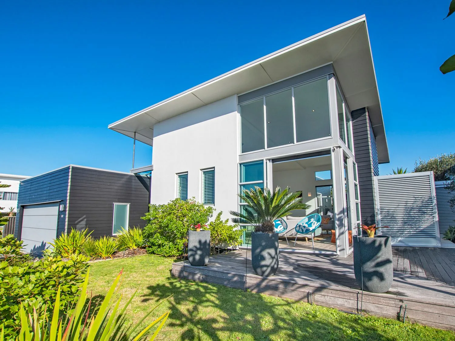 Modern house with large windows wooden deck and potted plants in the garden at Beachy on Bream - Ruakaka Holiday Home in Ruakaka