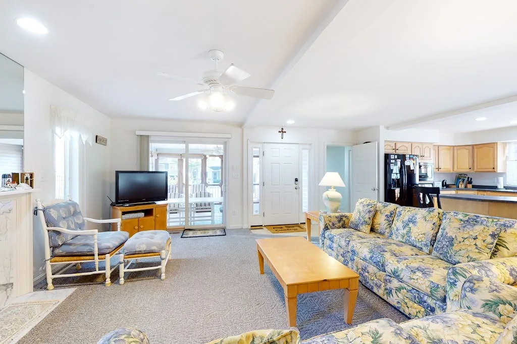 A bright living room with floral seating, a coffee table, and a television.
