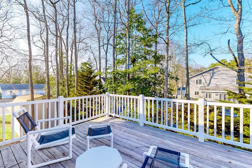 Outdoor deck with white railings, seating, and trees in the background.
