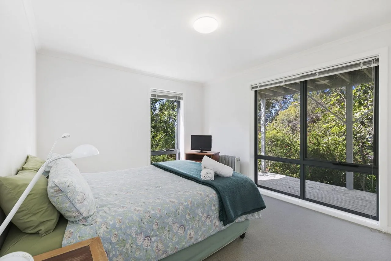 A bright bedroom with a bed and large windows overlooking trees.