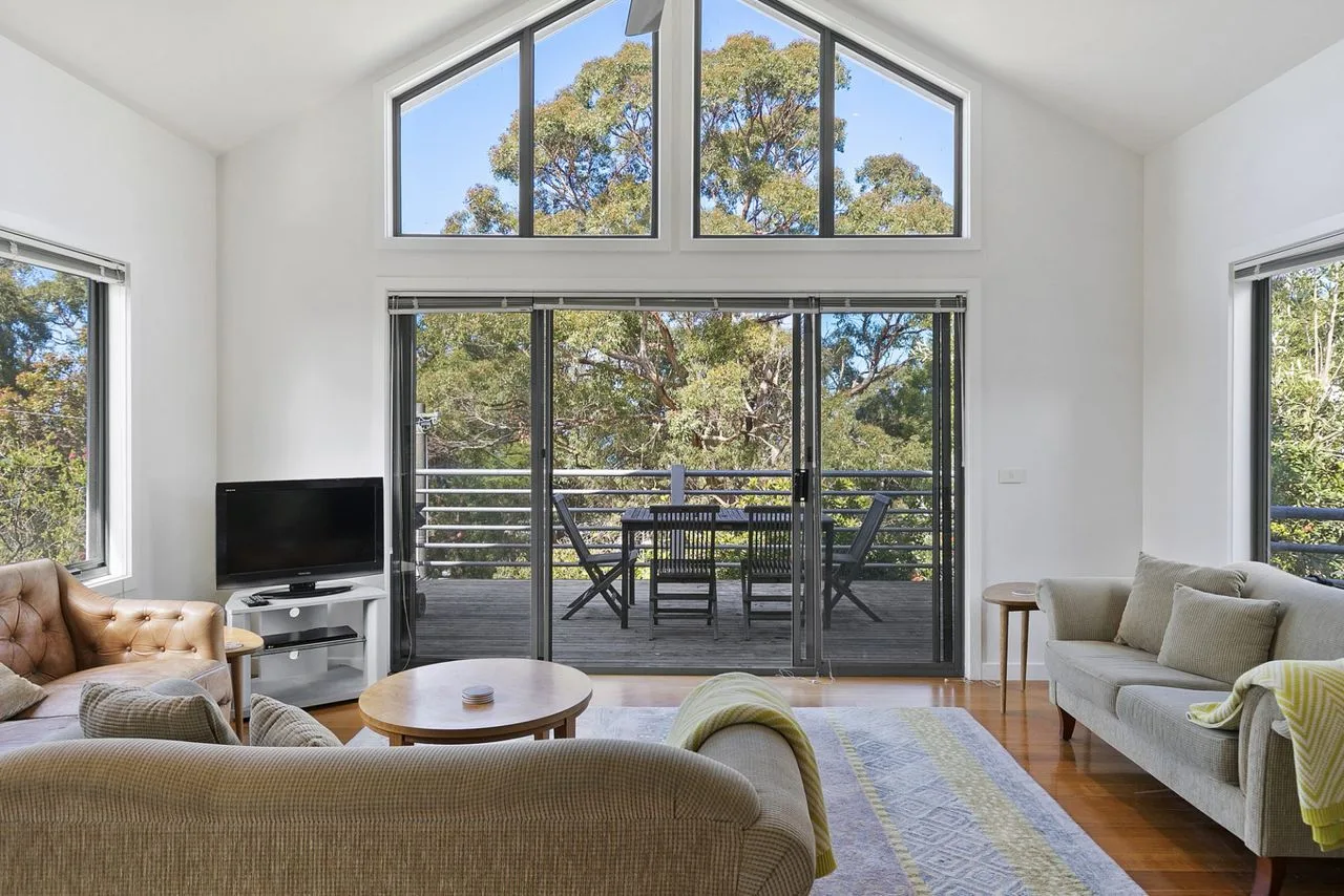 A bright living room opens onto a balcony with a dining table and chairs.