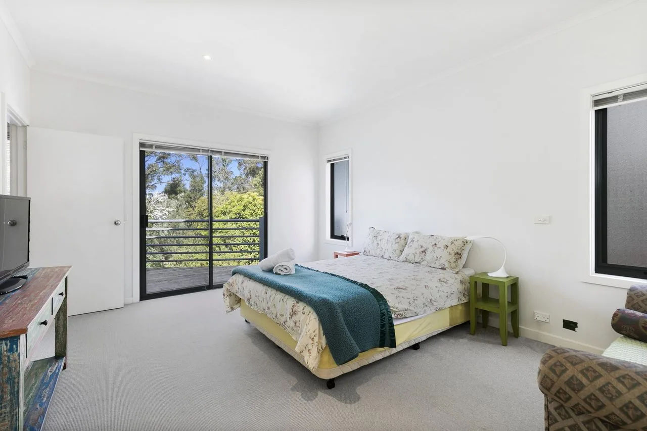 A bright bedroom with a bed beside a glass door opening onto a balcony.