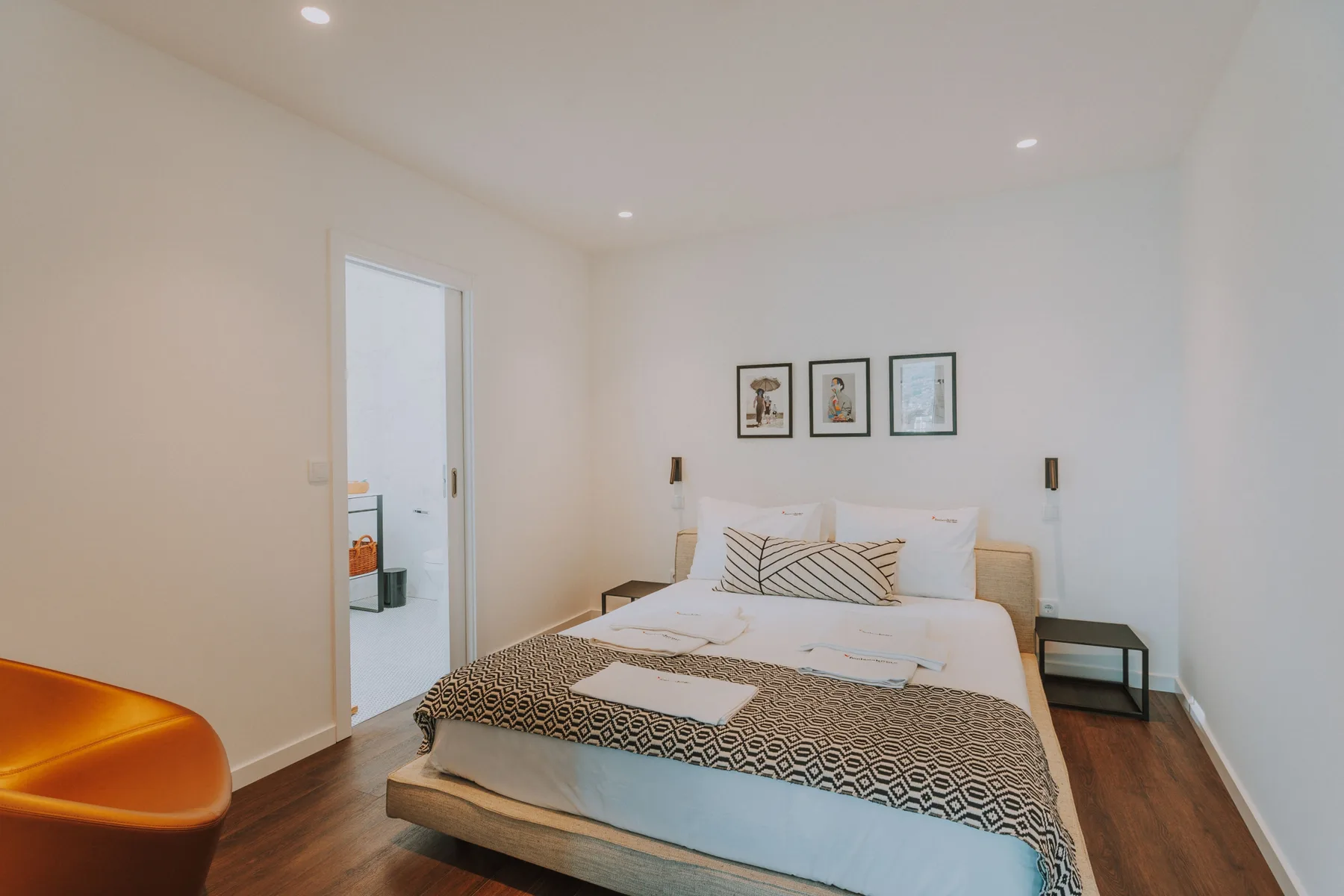 Un dormitorio luminoso con una cama tendida y cuadros enmarcados sobre ella.