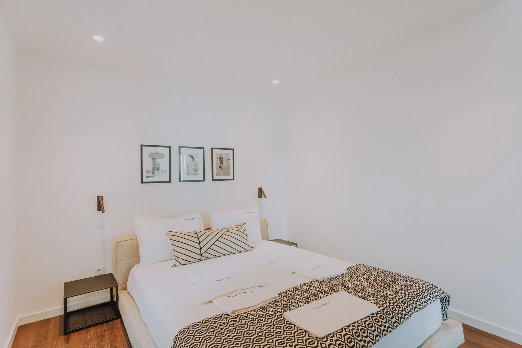 Un dormitorio luminoso con ropa de cama blanca y cuadros enmarcados sobre la cama.