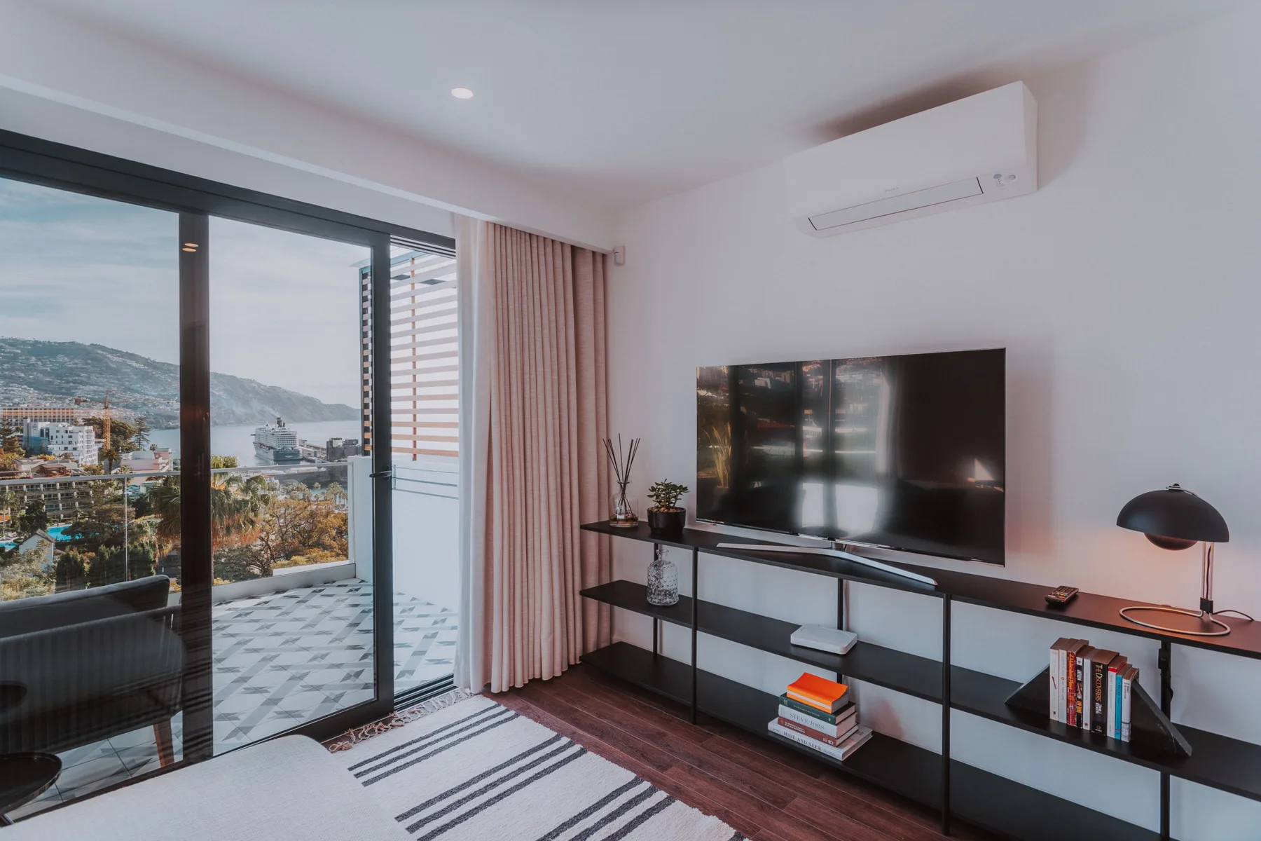 Sala de estar con un televisor sobre un mueble junto a puertas corredizas de vidrio.