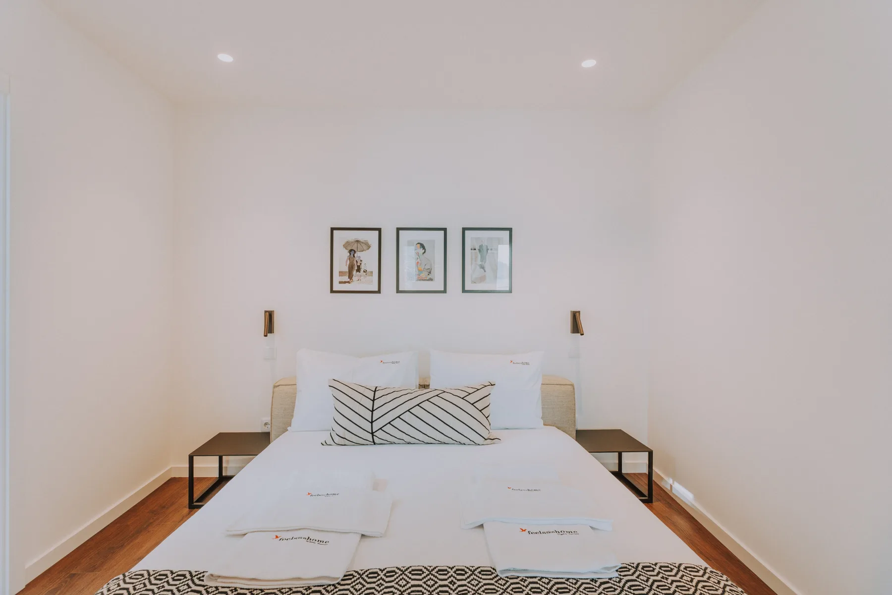 Un dormitorio con una cama, cojines decorativos y cuadros enmarcados encima.