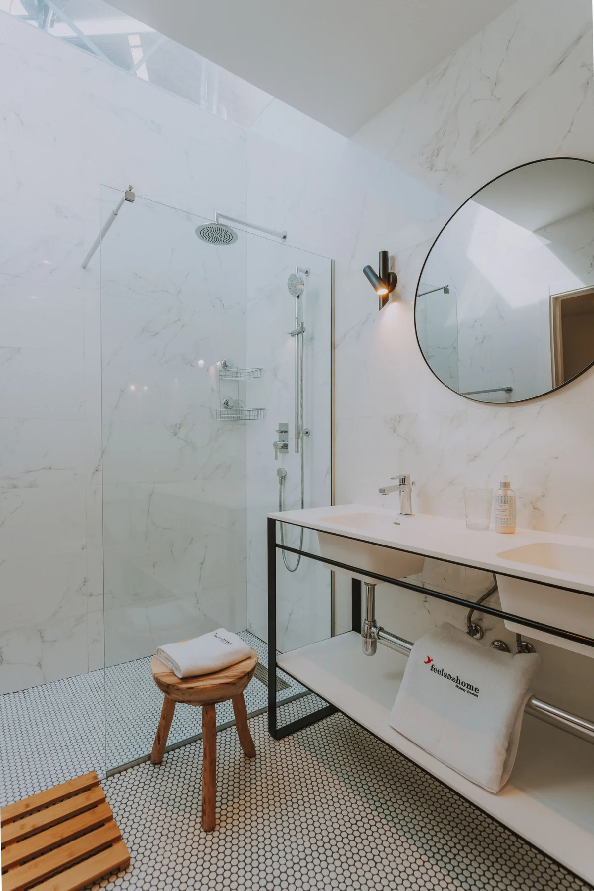 Un baño luminoso con ducha de vidrio, lavabo y espejo redondo.