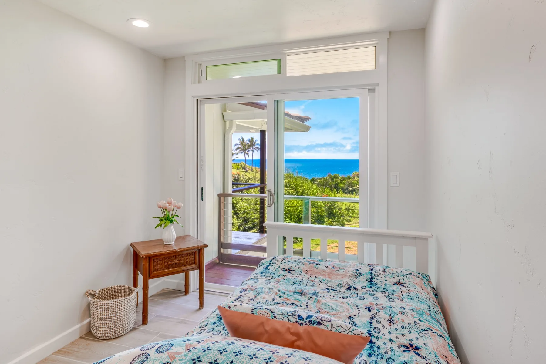 Un dormitorio con una colcha estampada junto a puertas de vidrio con vista al océano.