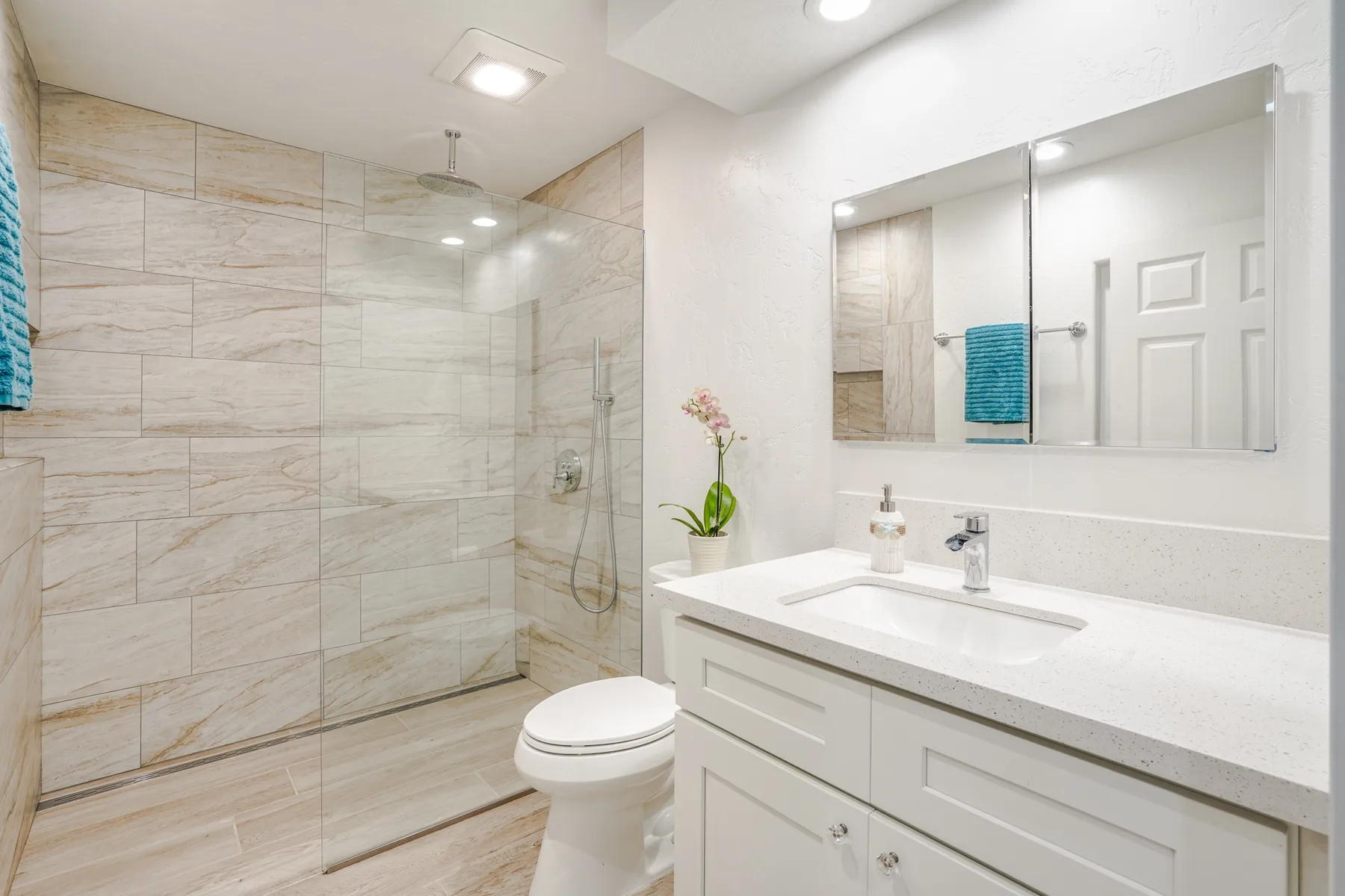 Un baño luminoso con una ducha de vidrio y un mueble de lavabo blanco.