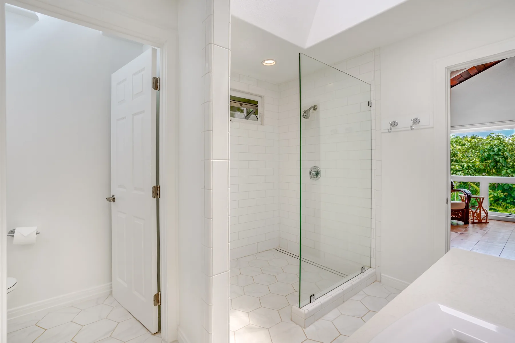 Un baño luminoso con una ducha de vidrio y una puerta abierta.