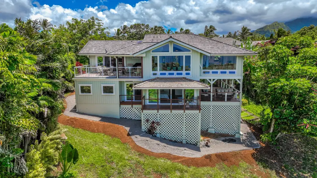 Una casa elevada con balcones está rodeada de exuberante vegetación tropical.