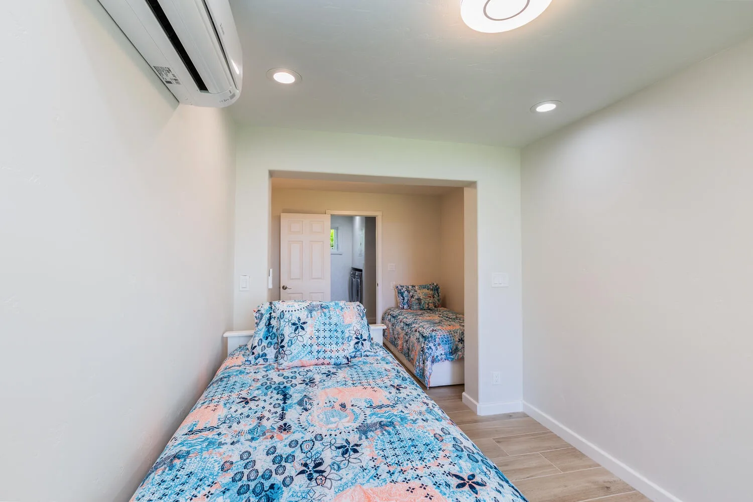 Un dormitorio con ropa de cama estampada en dos camas y un aire acondicionado en la pared.