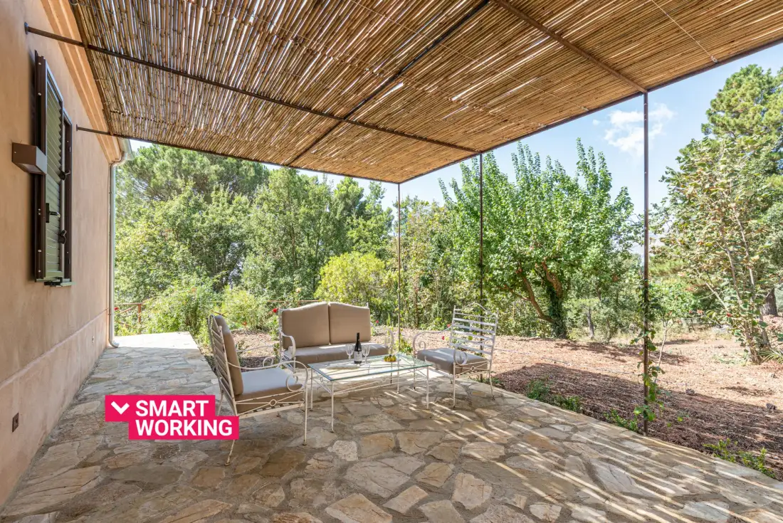 A shaded outdoor patio with seating and a leafy garden beyond.