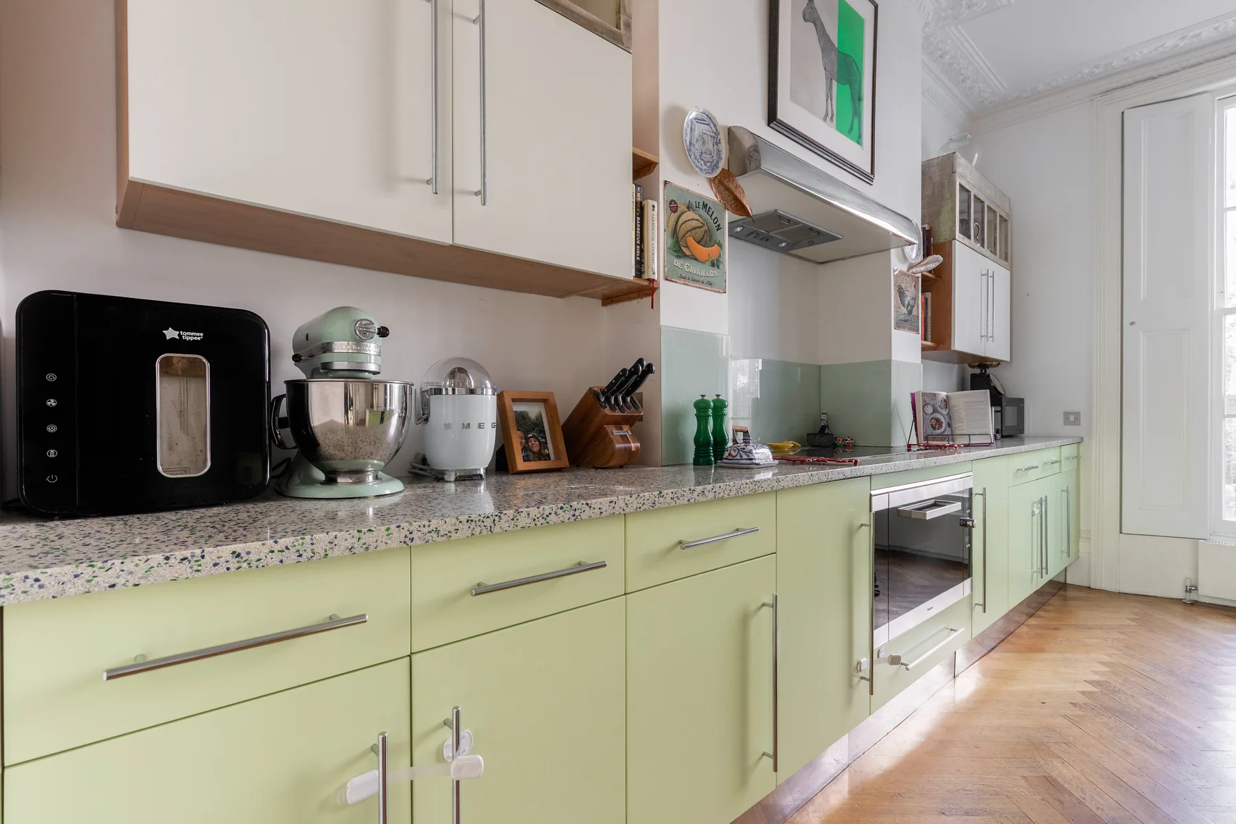 A bright kitchen with pale green cabinets, countertop appliances, and a built-in oven.