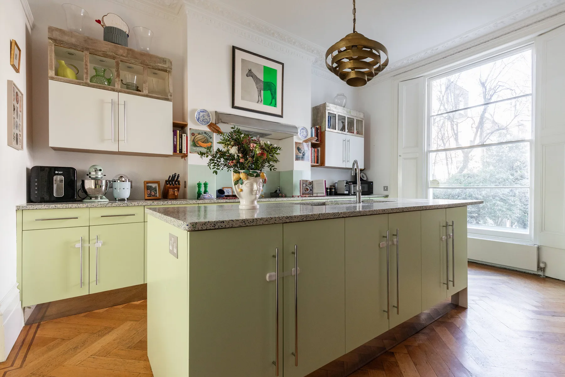 A bright kitchen with pale green cabinets, a central island, and a large window.