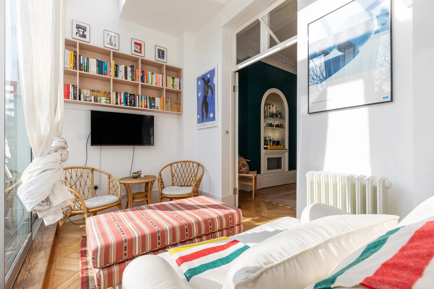 A bright living room with a striped ottoman, seating, and bookshelves.