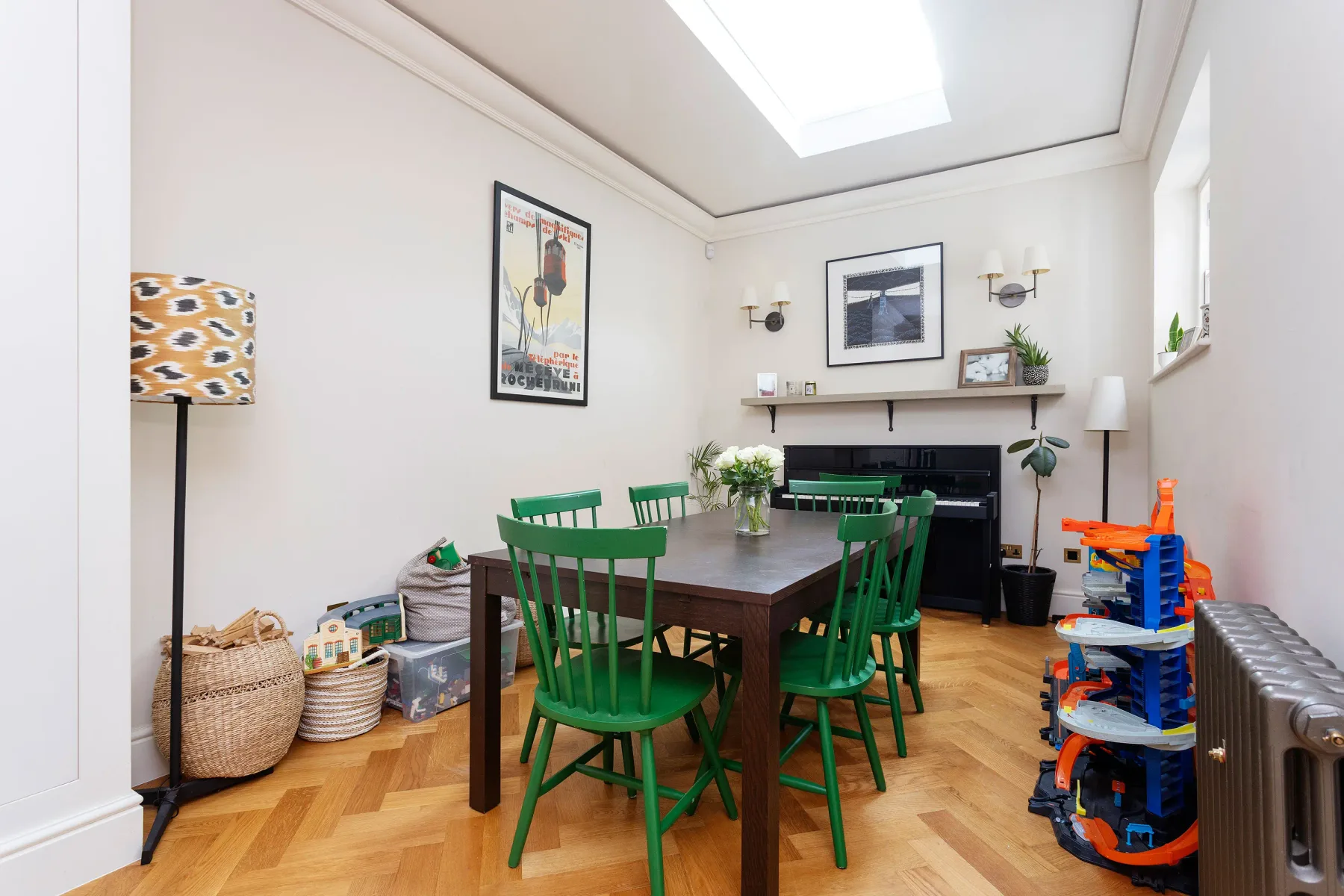 A dining room with a wooden table and green chairs beneath a skylight.