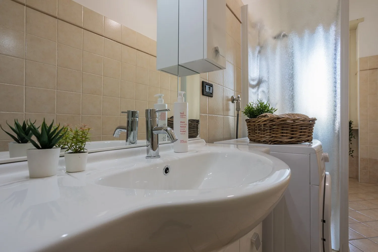 A bathroom sink and countertop sit in front of a curtained window.