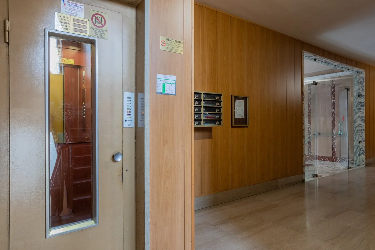 An indoor hallway with a wood-paneled wall and an elevator.