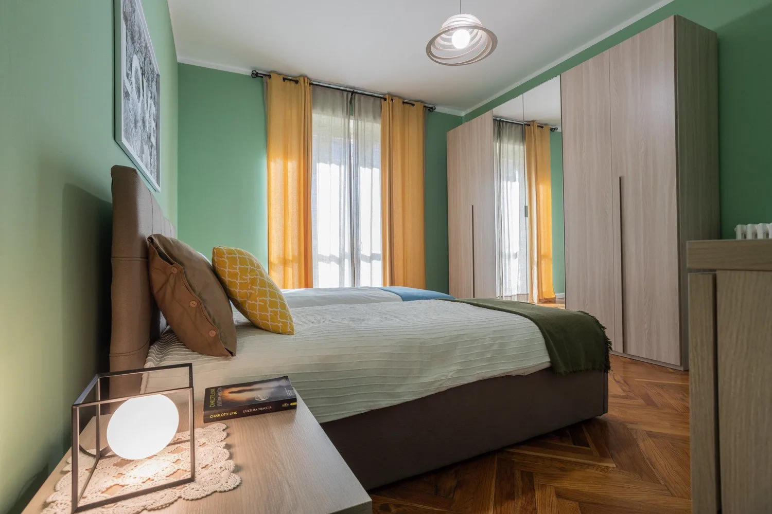 Un dormitorio con una cama tendida, cortinas mostaza y un armario grande.
