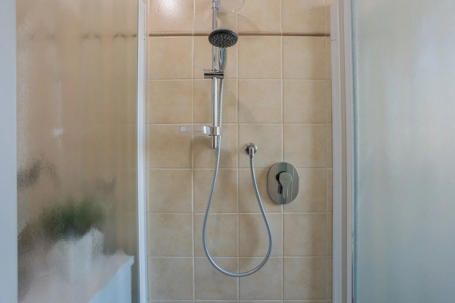 A tiled shower area with a handheld showerhead and hose.