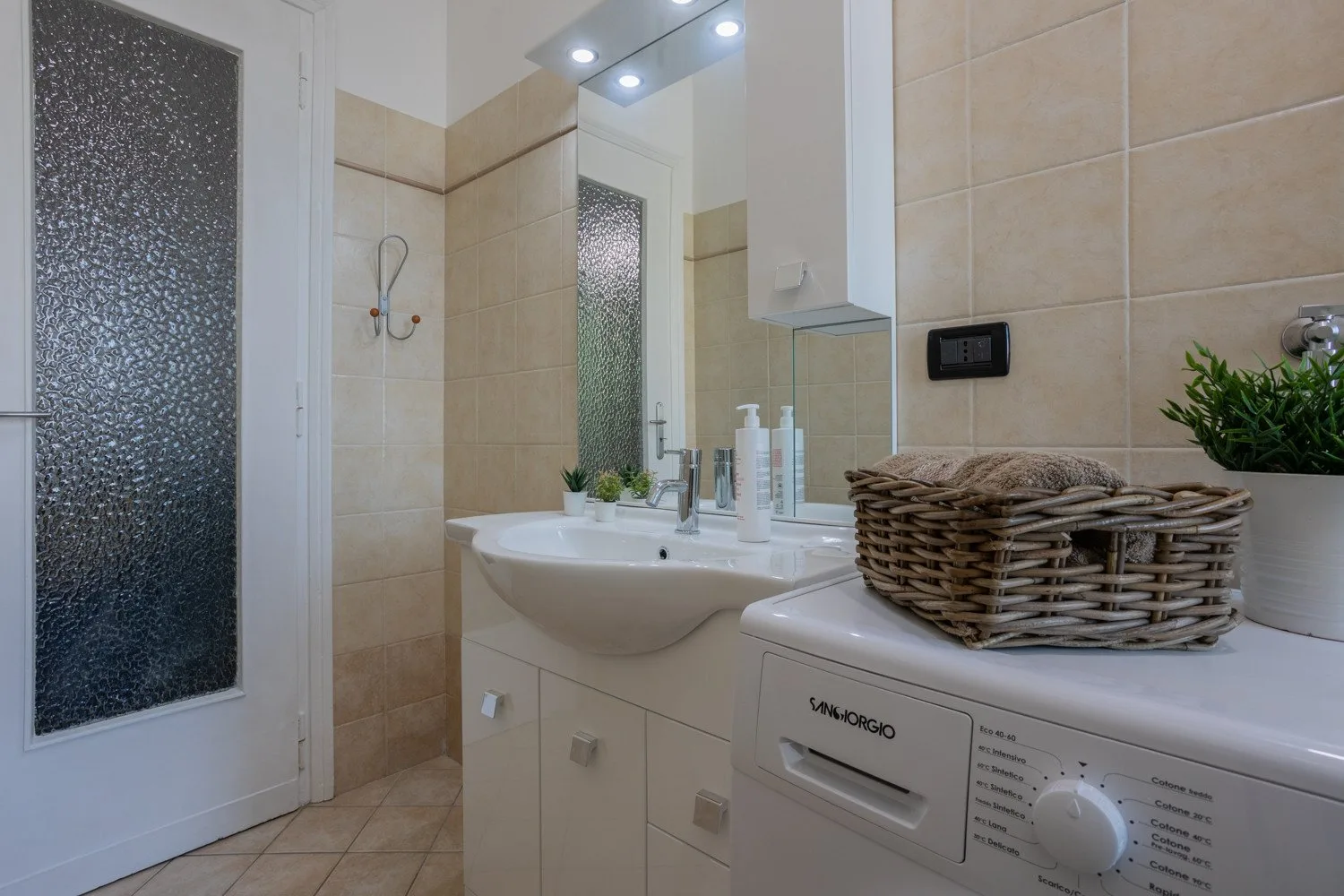 A tiled bathroom with a sink, mirror, and washing machine.