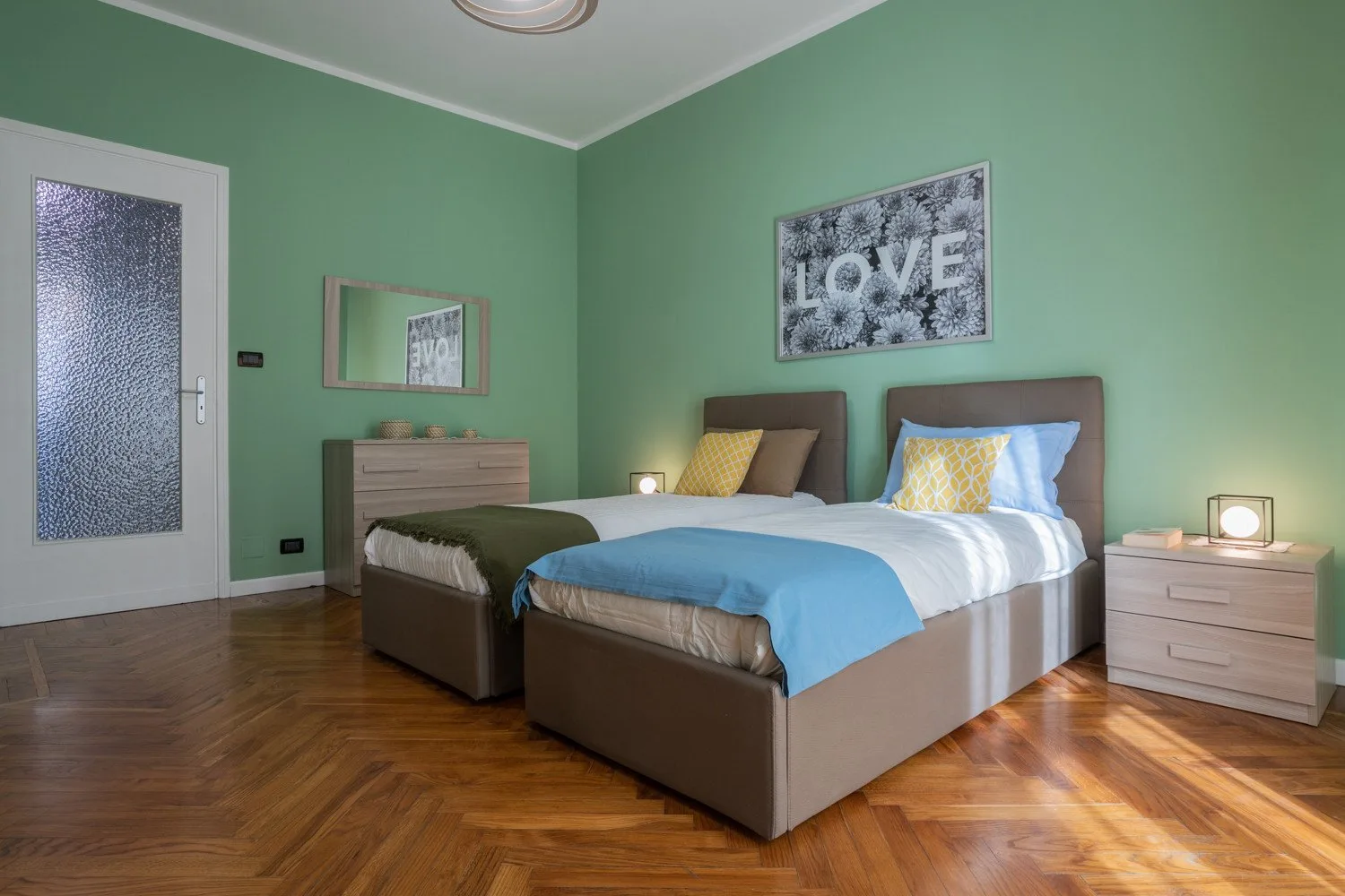 Un dormitorio con dos camas, paredes verdes y suelo de madera.