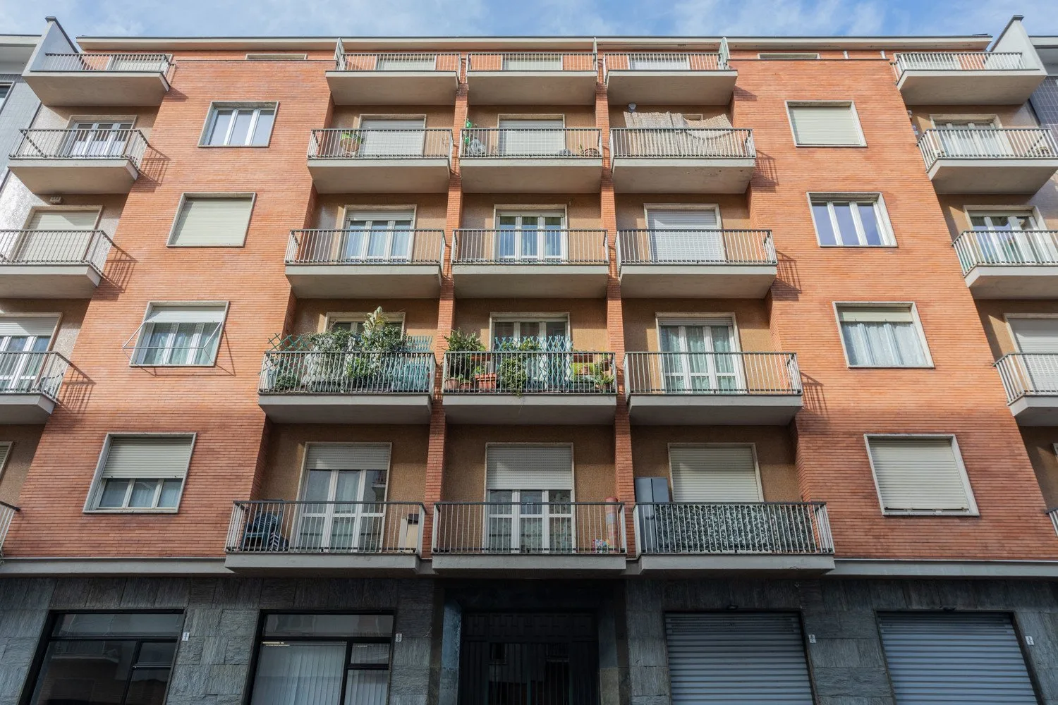 A brick apartment building facade with rows of balconies and windows.
