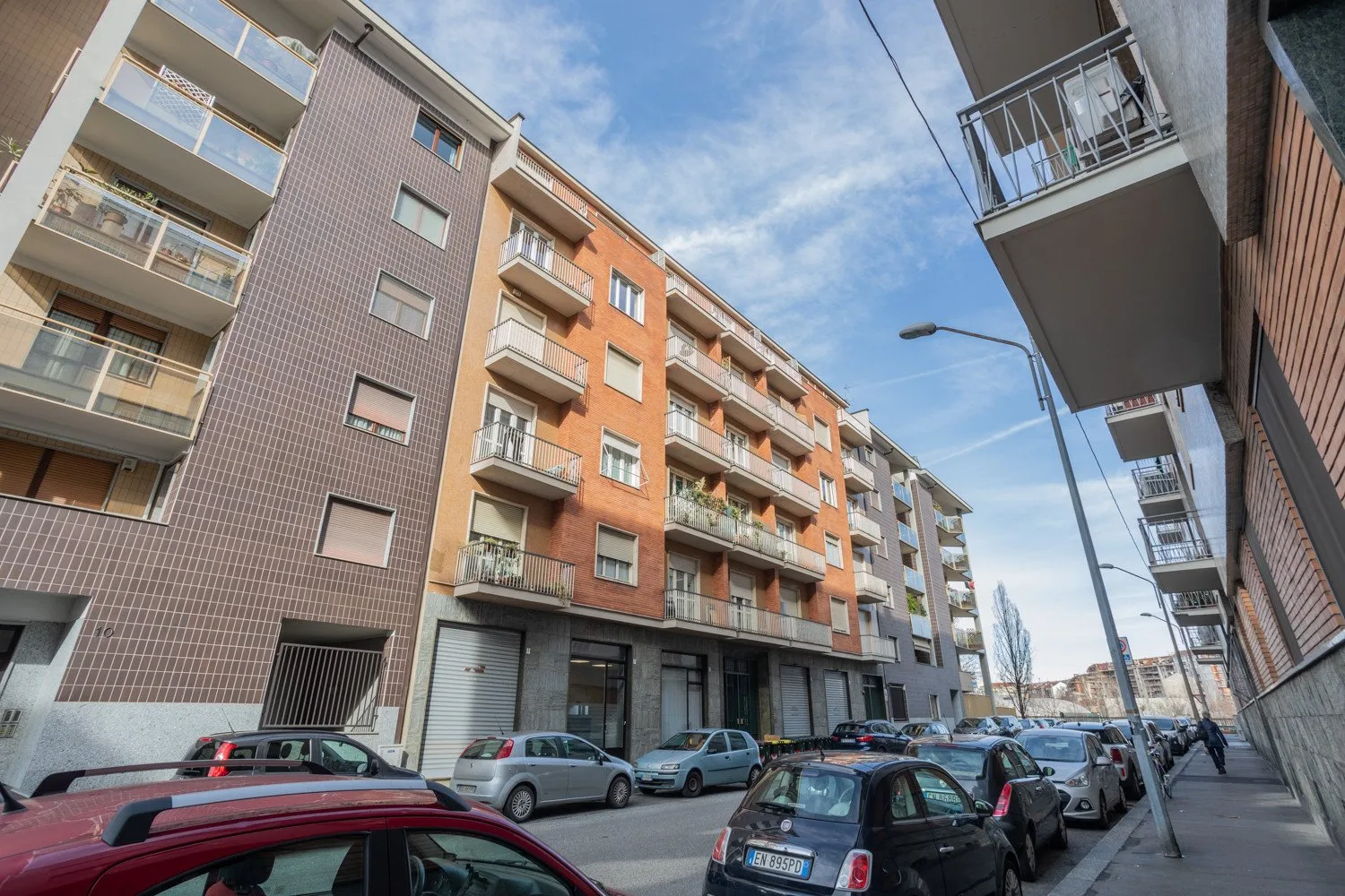 Apartment buildings line a city street under a partly cloudy sky.