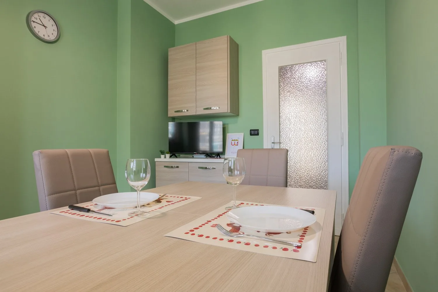 A dining area with a light wood table, place settings, and green walls.