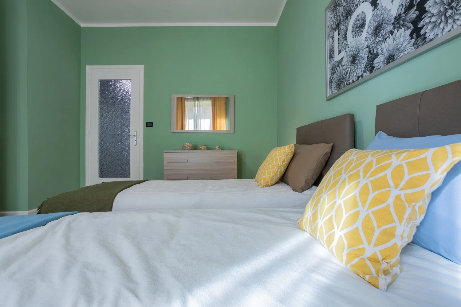 A bedroom with beds, yellow patterned pillows, and green walls.
