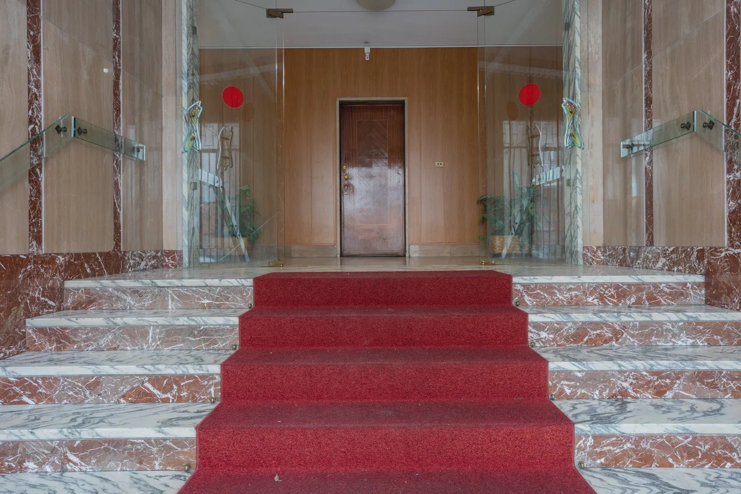 A formal entrance hall with a red carpeted staircase leading to a wooden door.