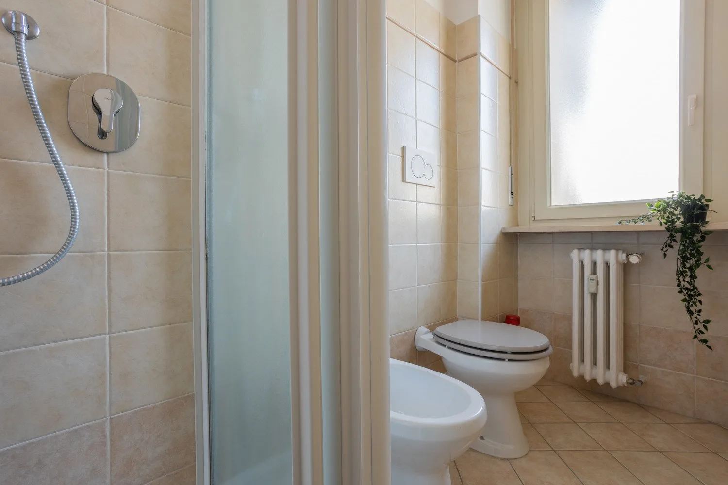 A tiled bathroom with a shower, toilet, and bright window.