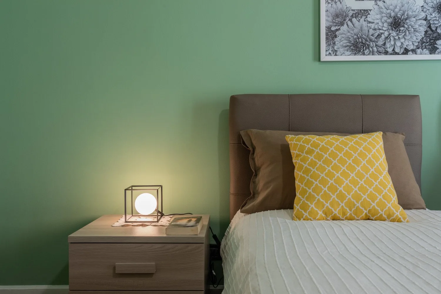 A bedroom with a neatly made bed beside a bedside table and lamp.