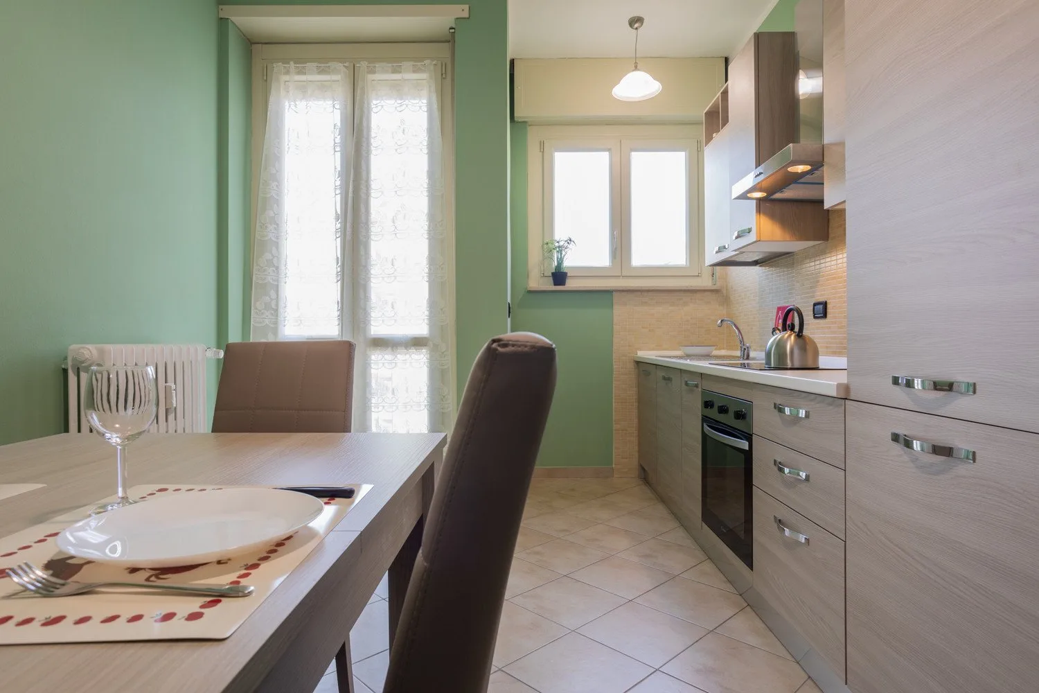 A dining area beside a kitchen, with a table set by tall windows.