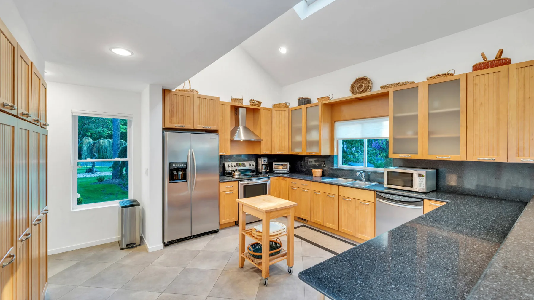 Una cocina luminosa con gabinetes de madera, electrodomésticos de acero inoxidable y una isla central.