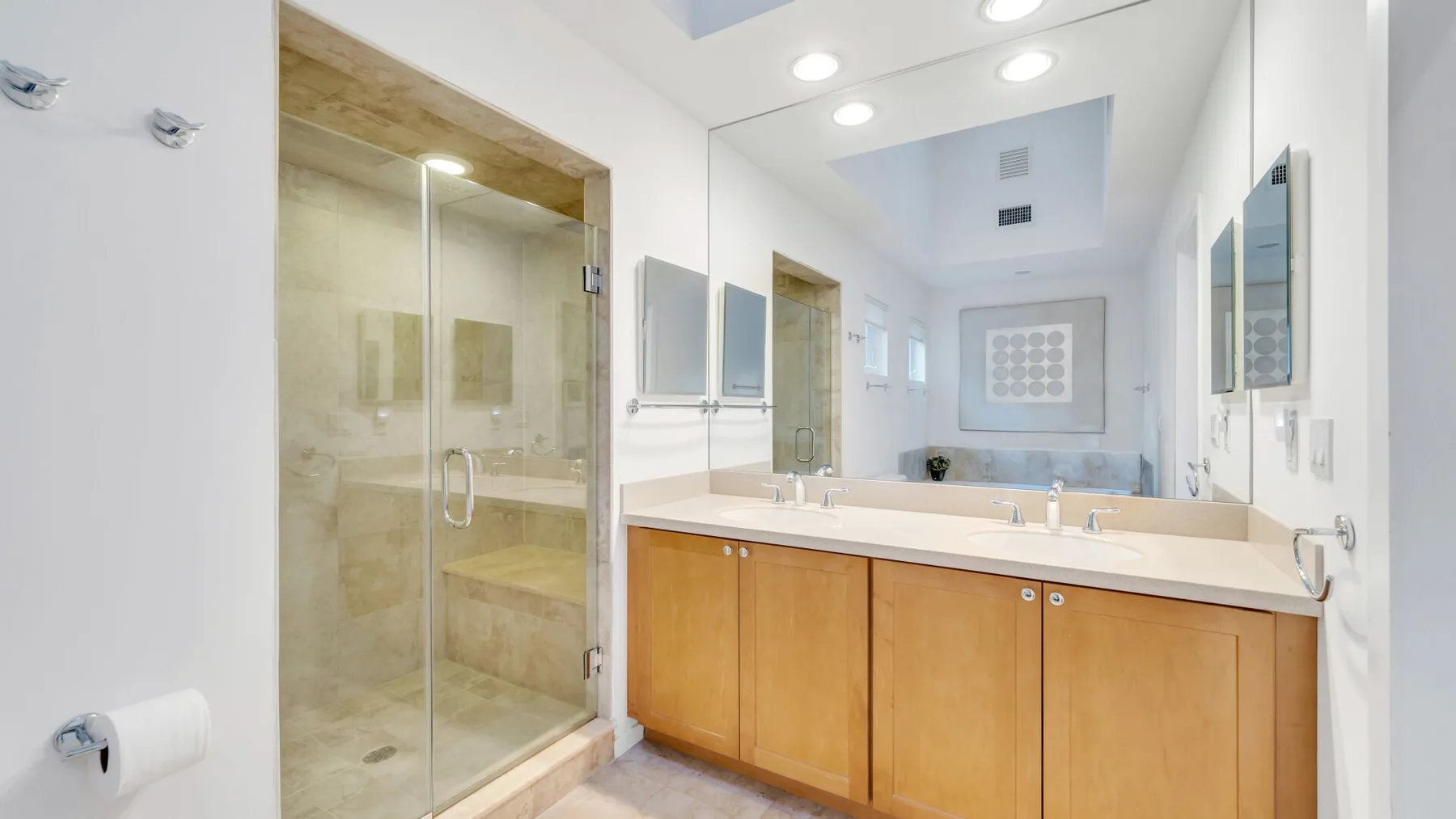 Un baño luminoso con un largo tocador y una ducha con mampara de vidrio.