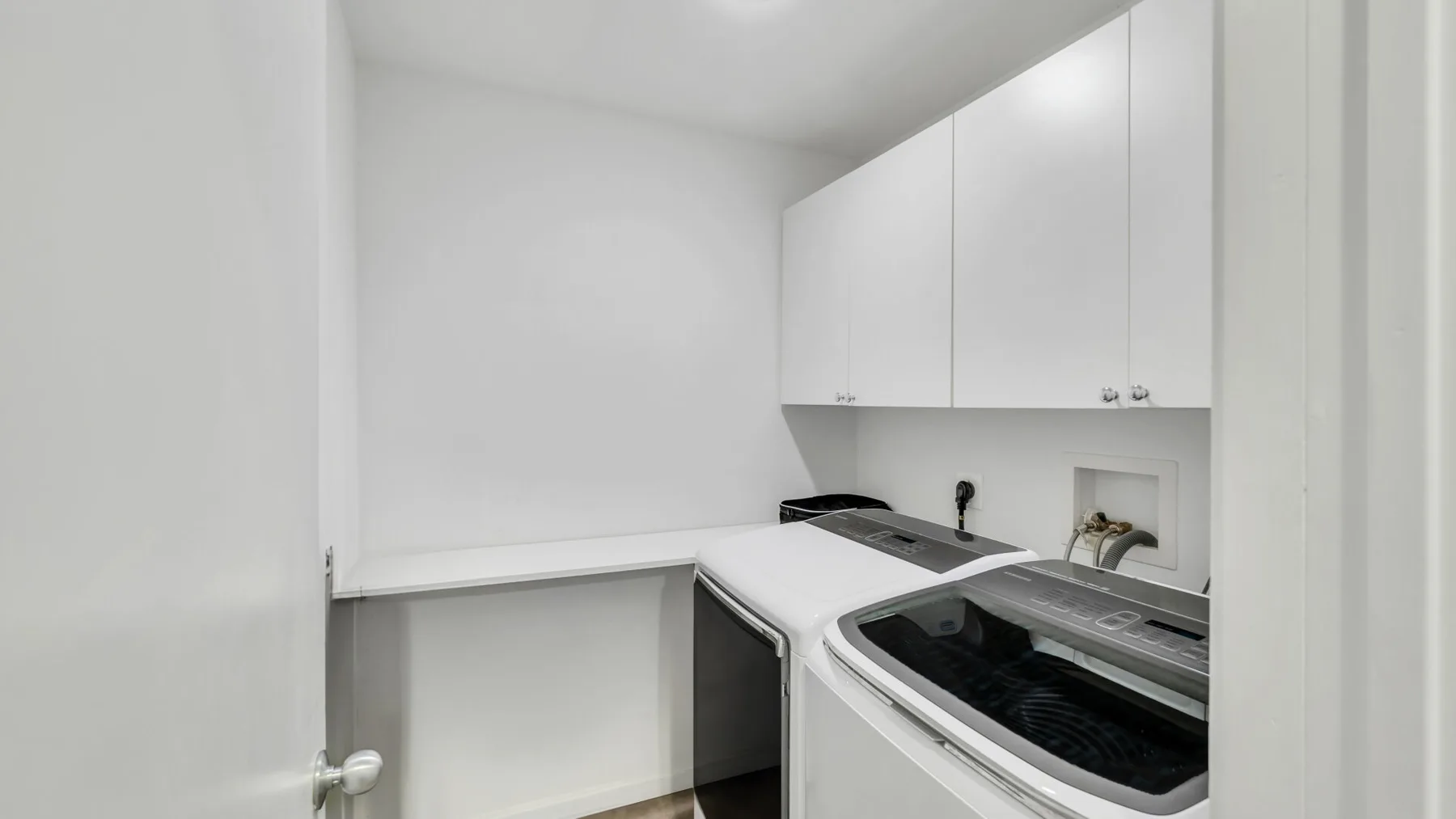 Un cuarto de lavado con lavadora y secadora bajo armarios blancos.