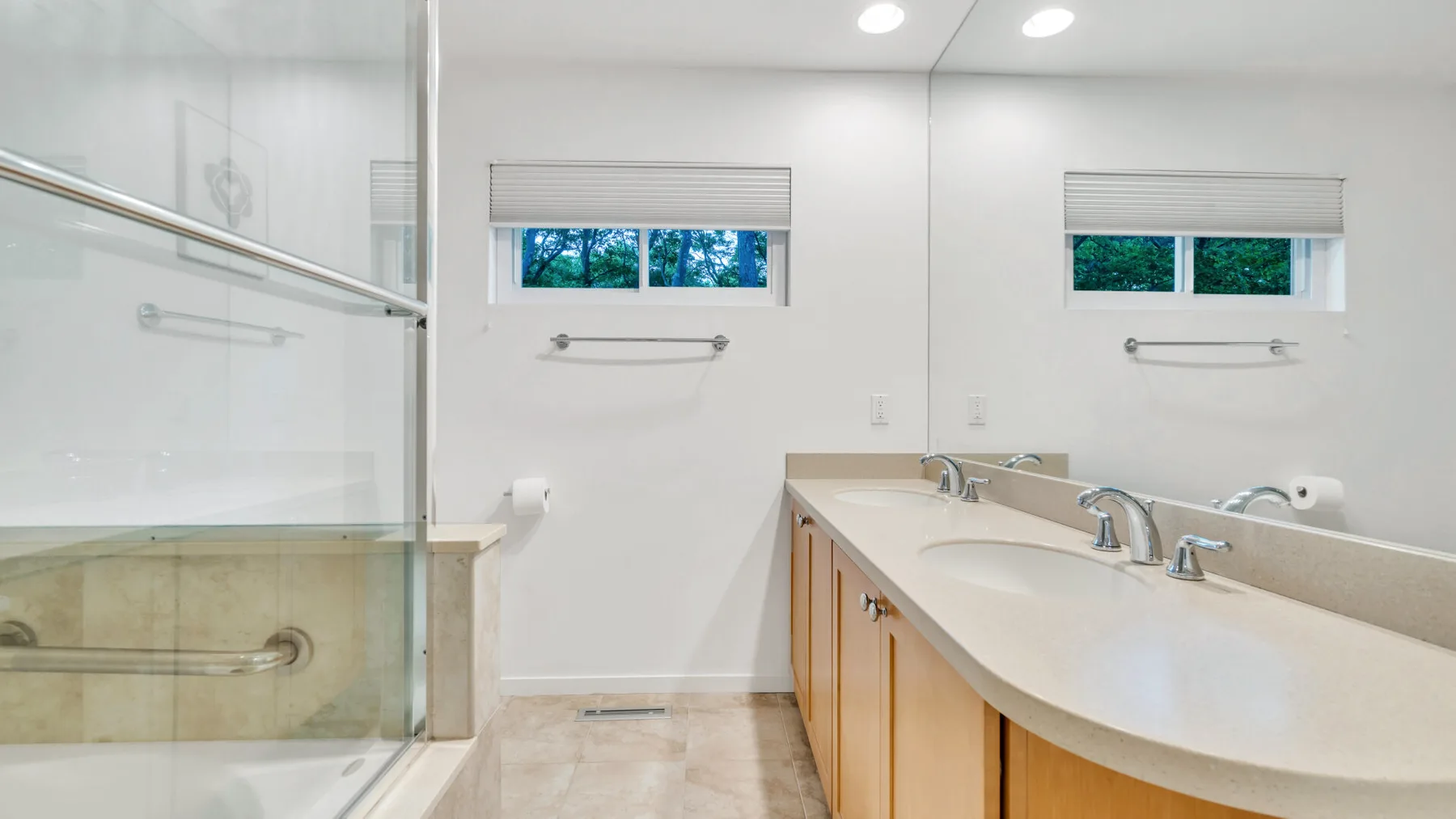 Un baño luminoso con un tocador largo y una ducha con mampara de vidrio.