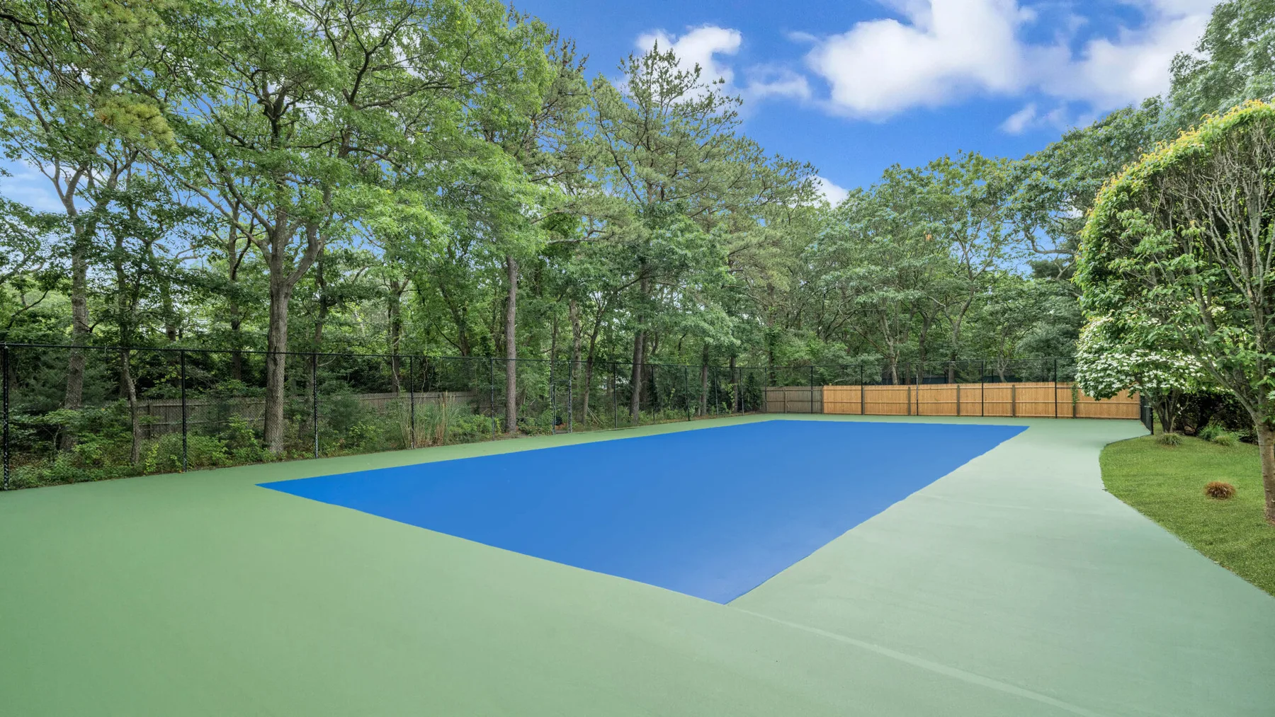 Una cancha de tenis azul está rodeada de árboles verdes y una cerca.